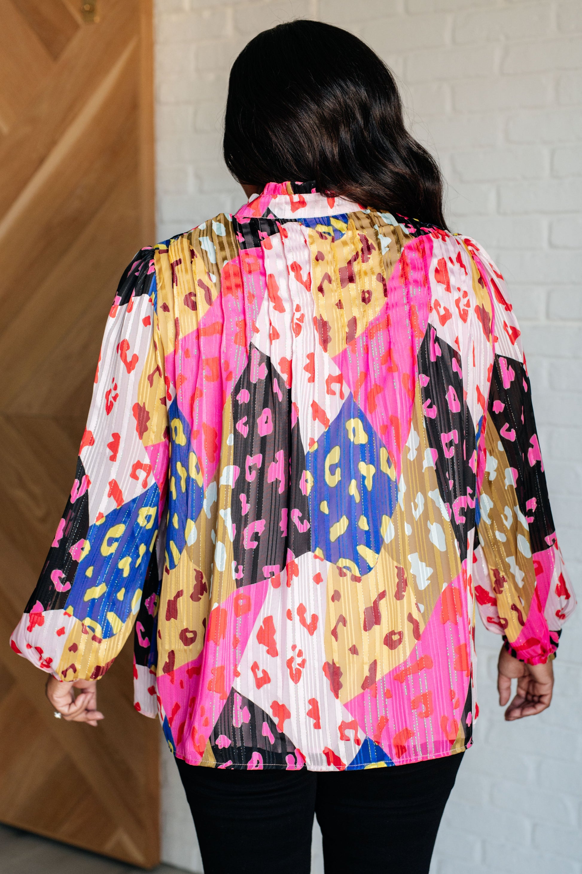 Person wearing a colorful patterned blouse with a white brick wall background