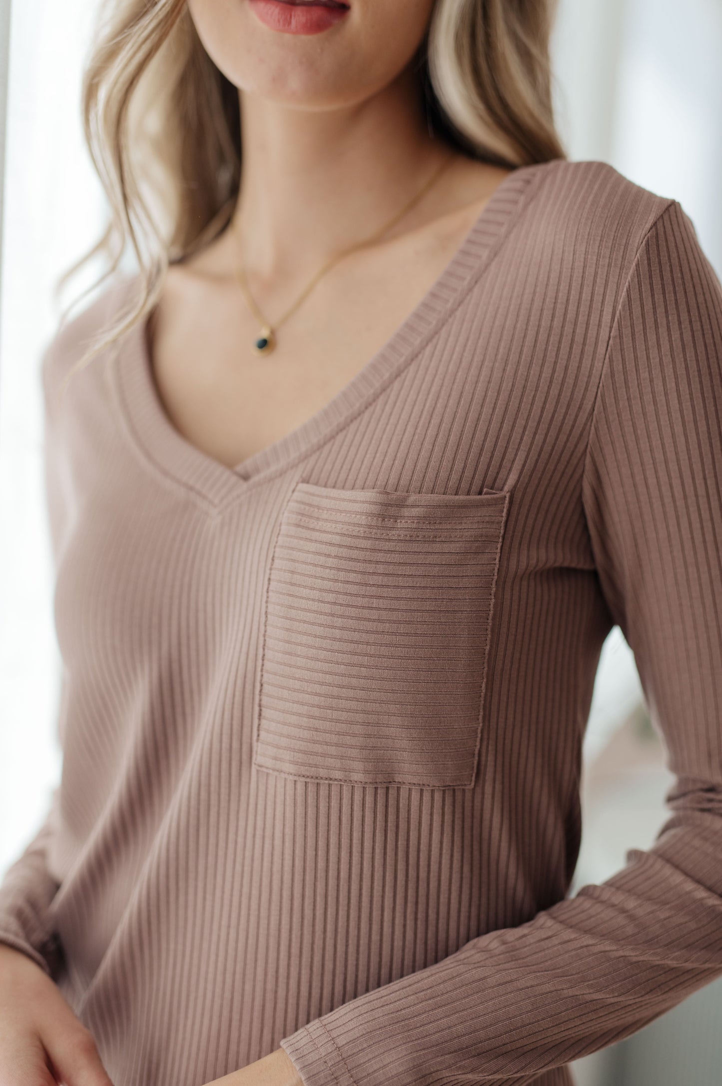 Close-up of a person wearing a ribbed brown long-sleeve top with a pocket.