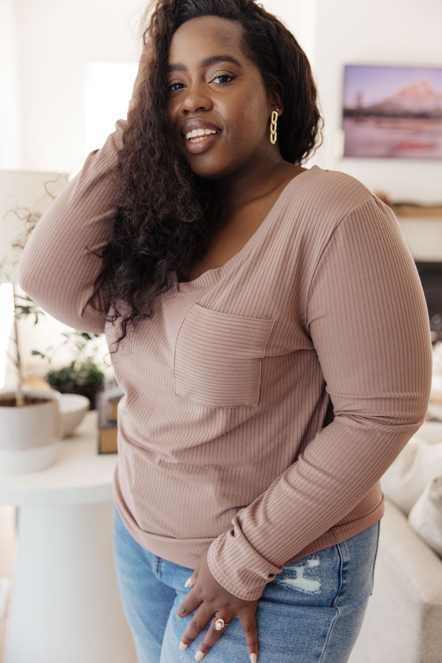 Woman wearing a beige long-sleeve top and blue jeans indoors.