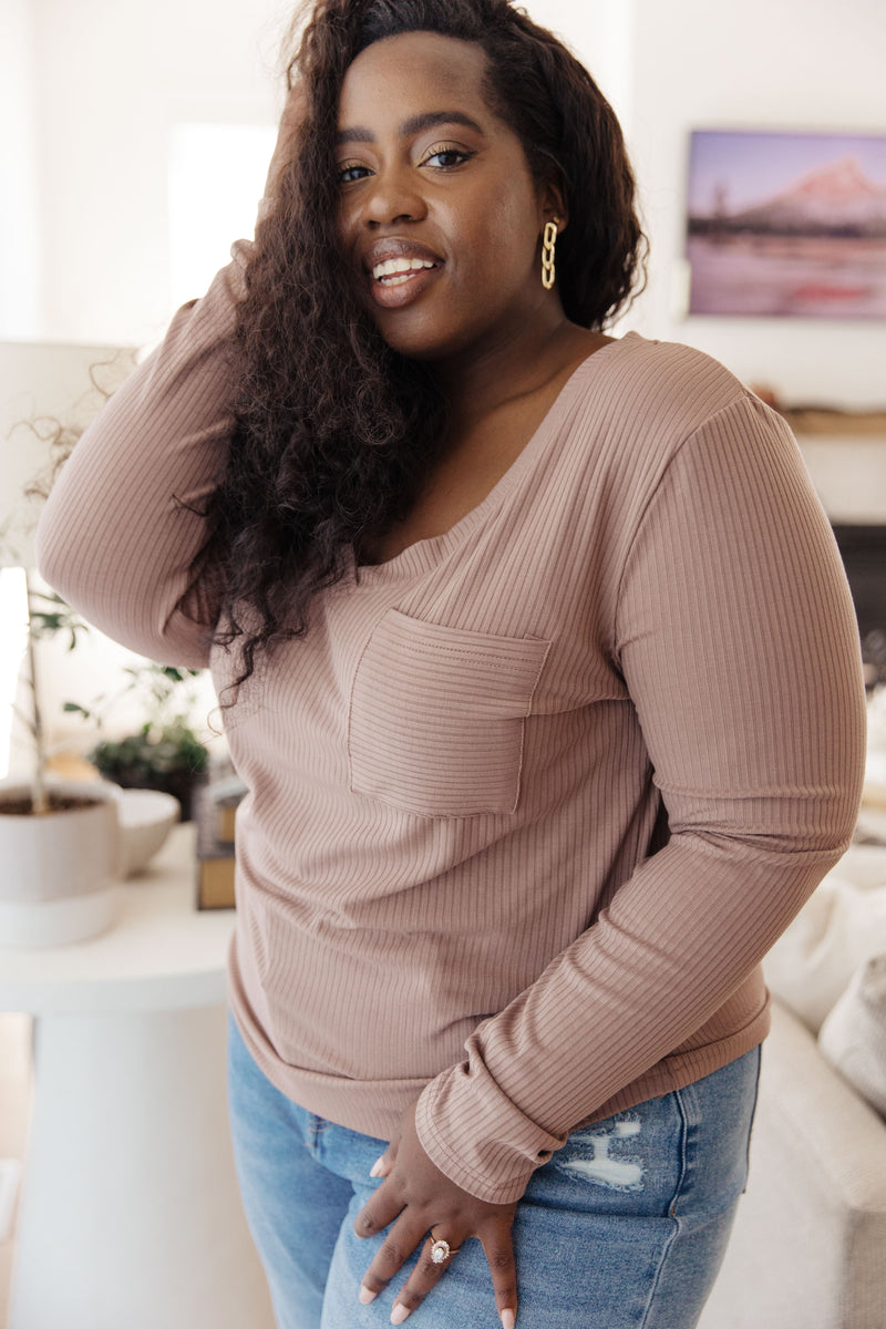 Woman wearing a beige long-sleeve top and blue jeans indoors.