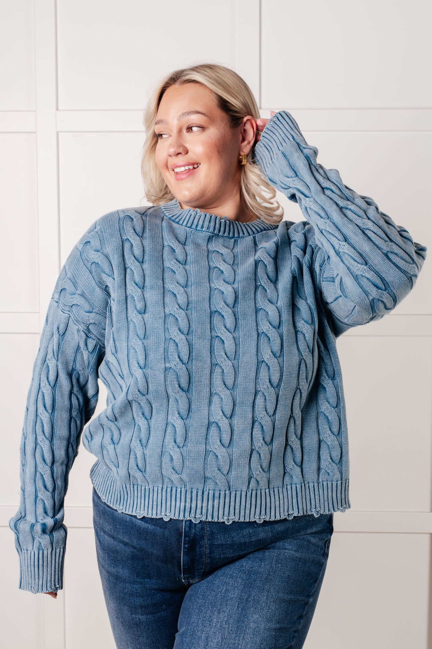 Woman wearing a blue cable knit sweater against a white tiled wall.