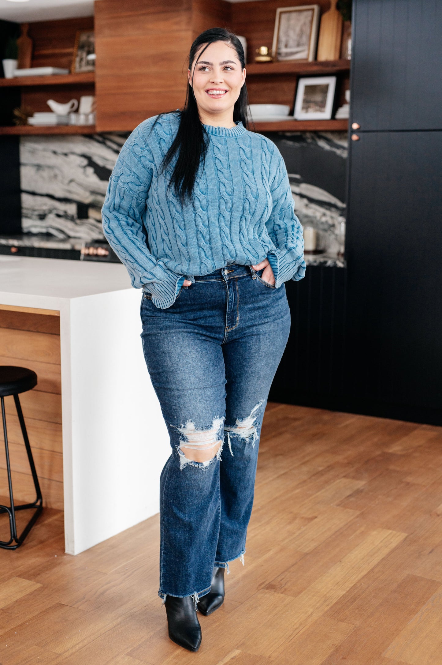 Woman wearing a blue sweater and jeans standing in a modern kitchen.