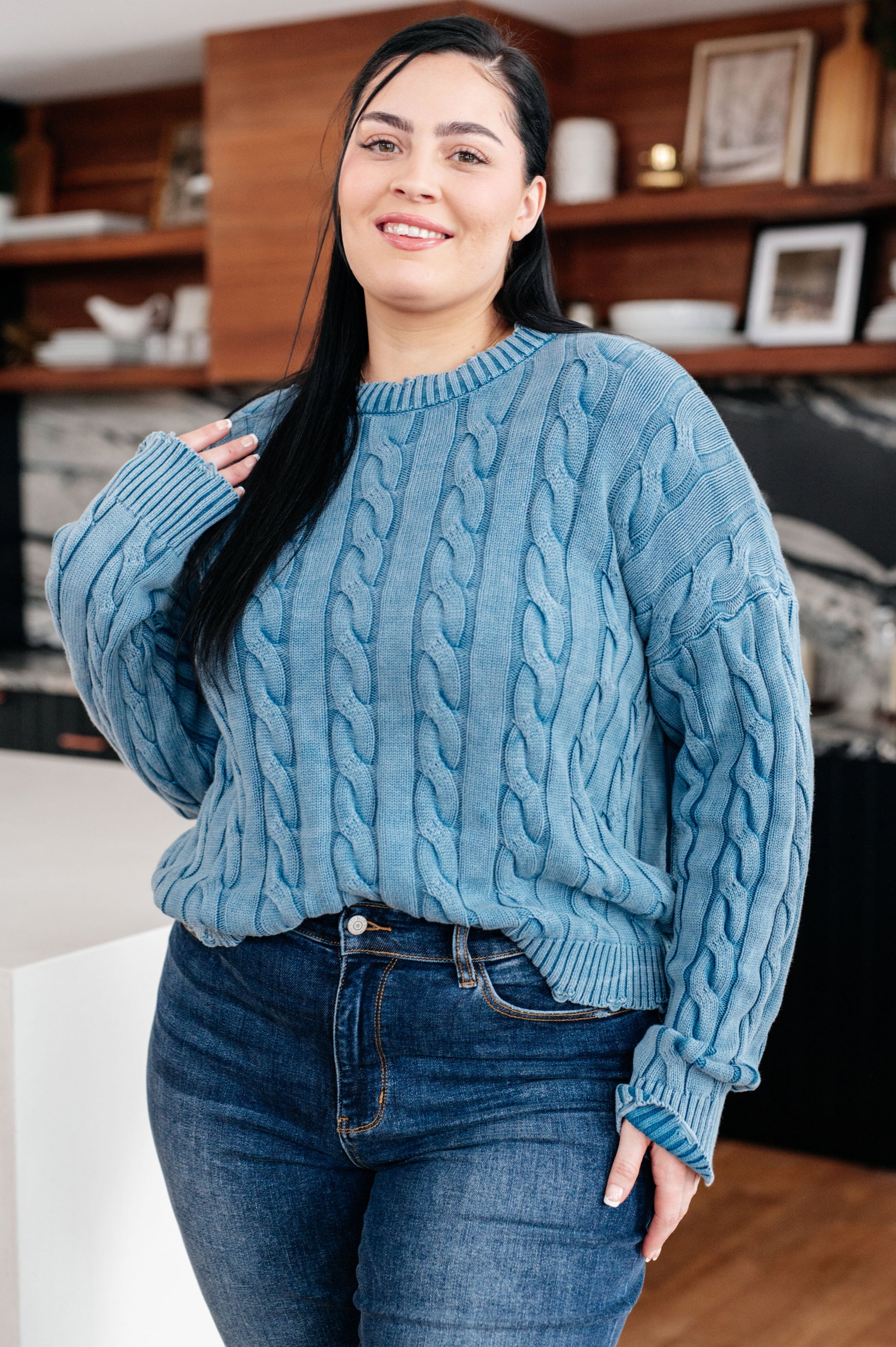 Woman wearing a blue cable knit sweater and jeans indoors.