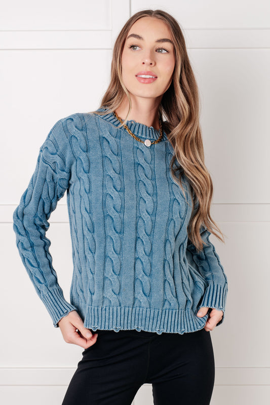 Woman wearing a blue cable knit sweater against a white background