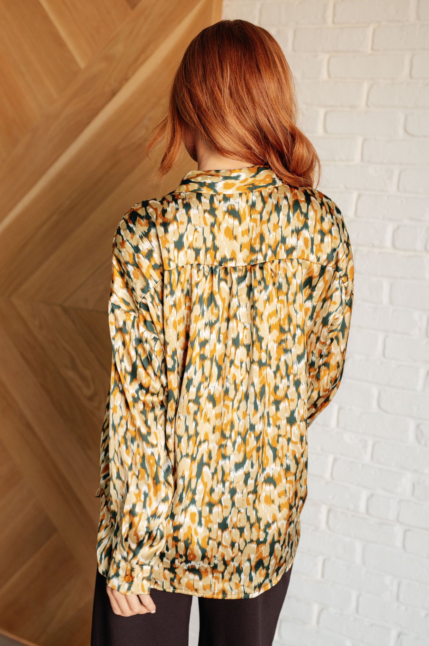 Person wearing a patterned blouse against a white brick wall.