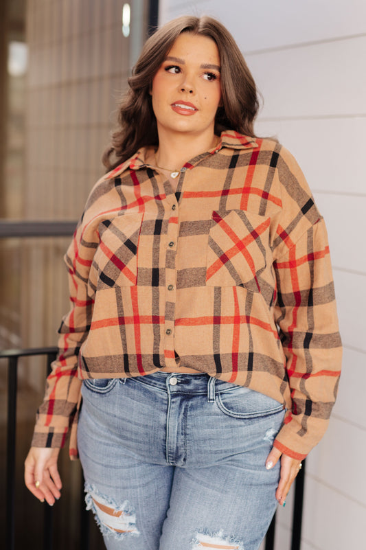 Woman wearing a plaid shirt and jeans standing against a white wall.