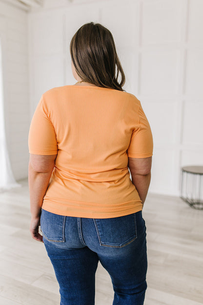 Person wearing an orange ribbed top and blue jeans standing in a minimalistic room.
