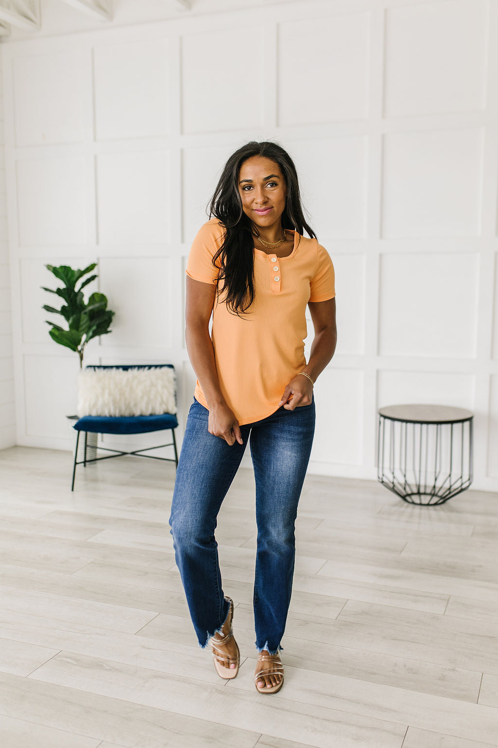 Woman wearing a yellow top and blue jeans standing in a modern room with white walls and wooden floor.