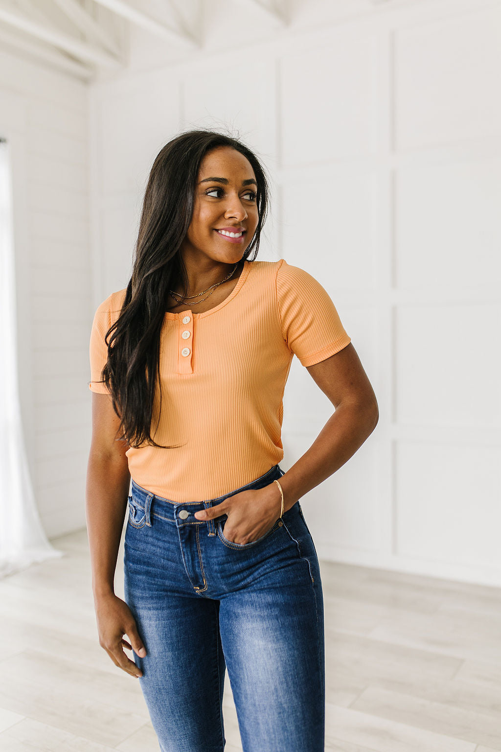 Woman wearing an orange top and blue jeans standing in a bright room.