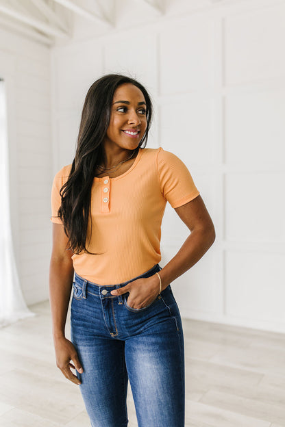 Woman wearing an orange top and blue jeans standing in a bright room.