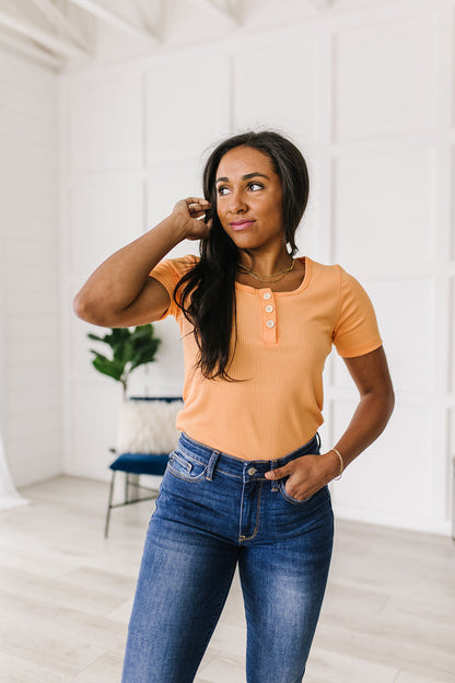 Woman wearing an orange shirt and blue jeans in a white room.