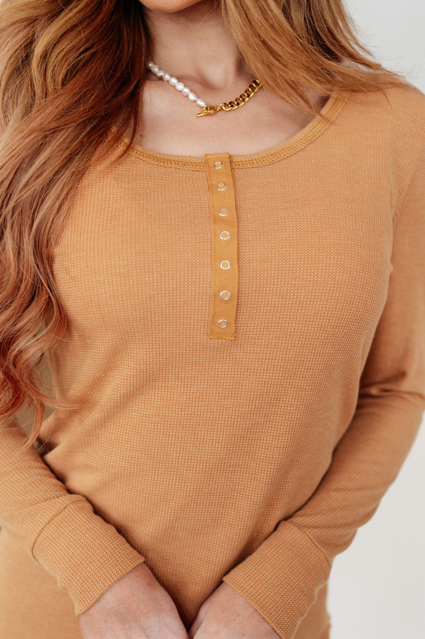 Person wearing a mustard yellow long-sleeve shirt with a plain background