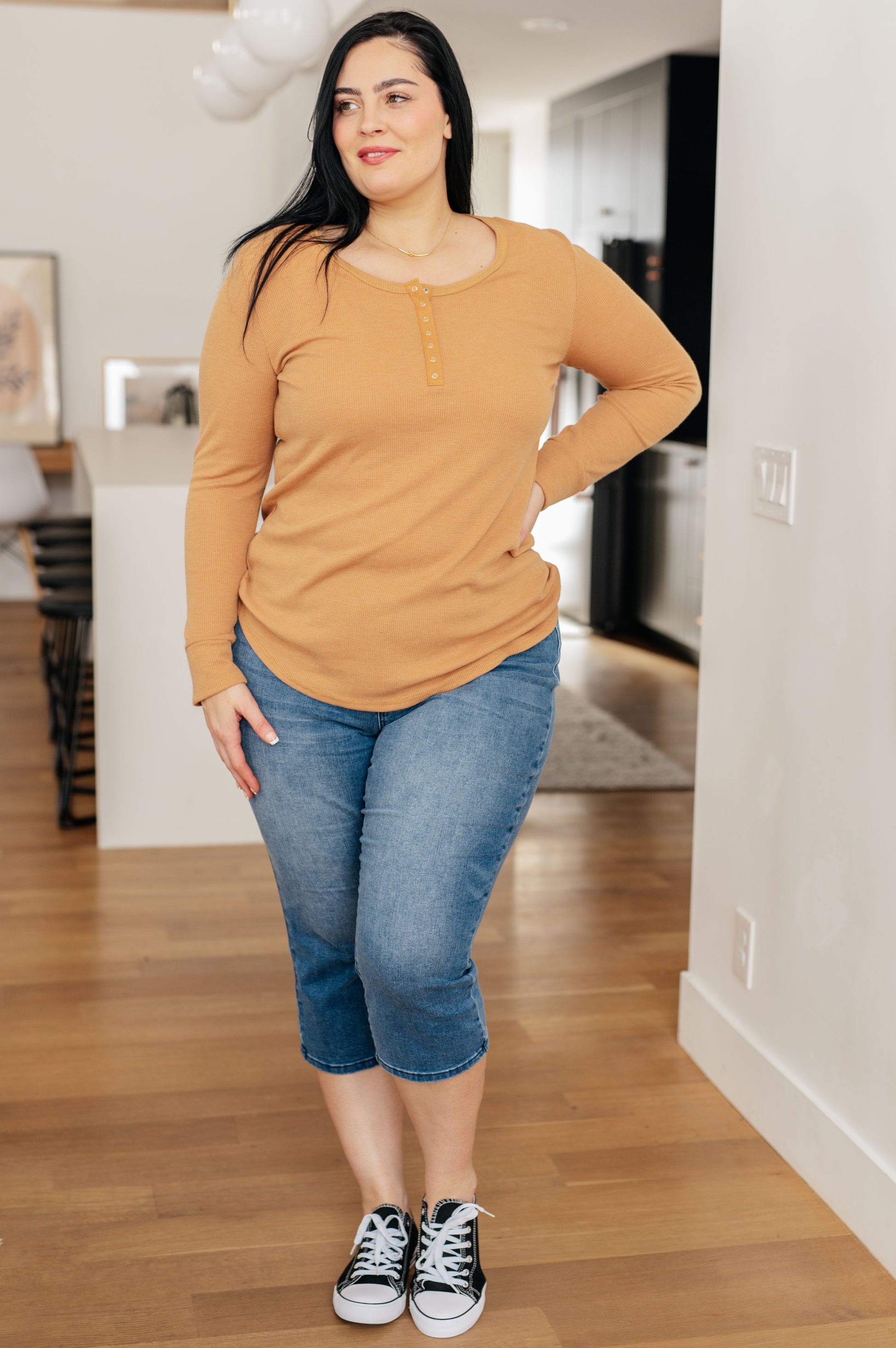 Woman wearing a mustard yellow long-sleeve top and blue jeans standing in a kitchen.
