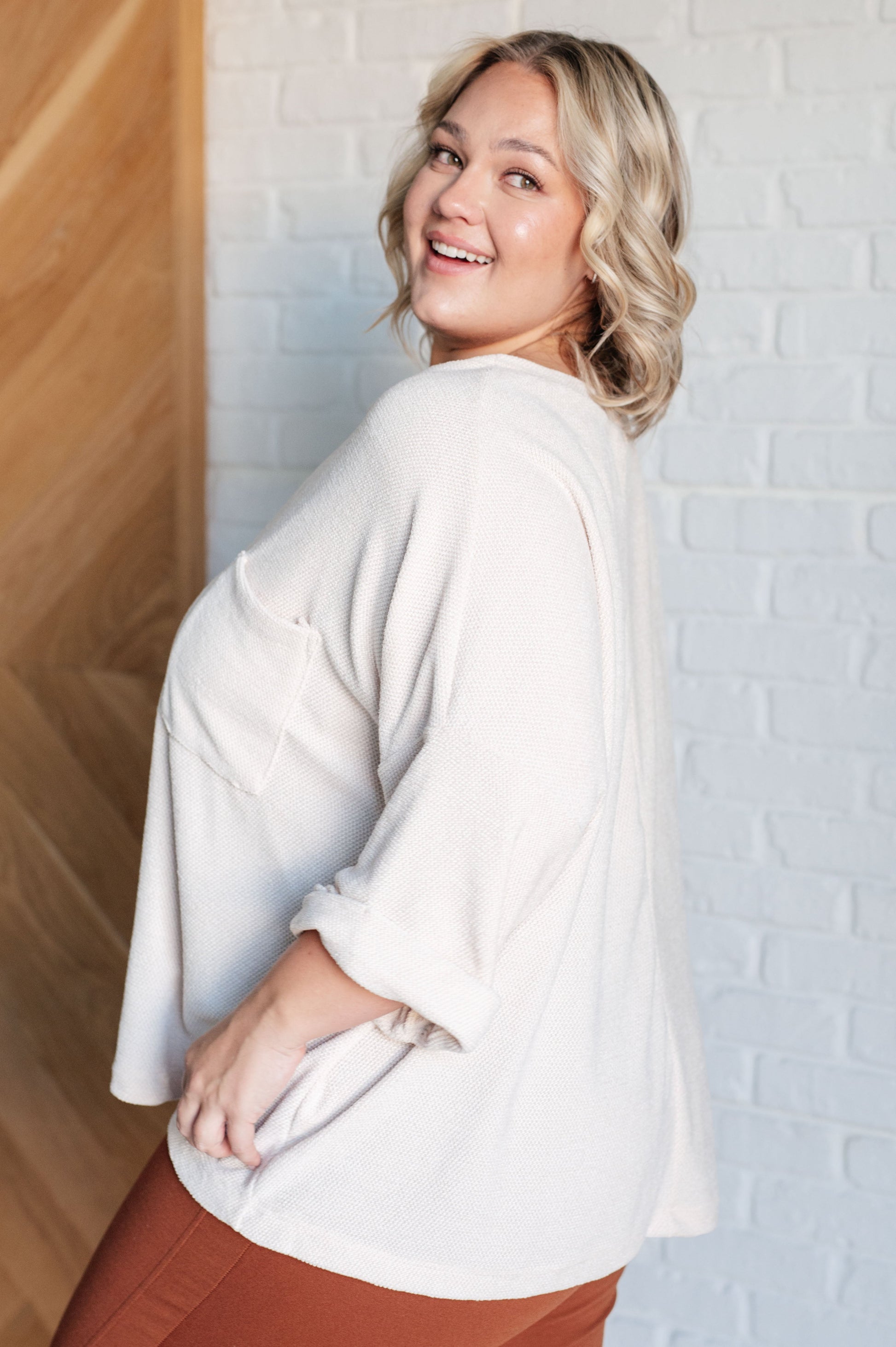 Woman wearing a white sweater against a light brick wall.