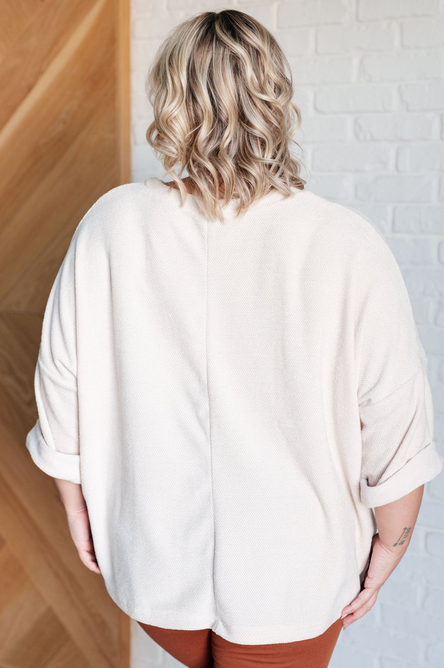 Person wearing a beige oversized shirt in a minimal indoor setting