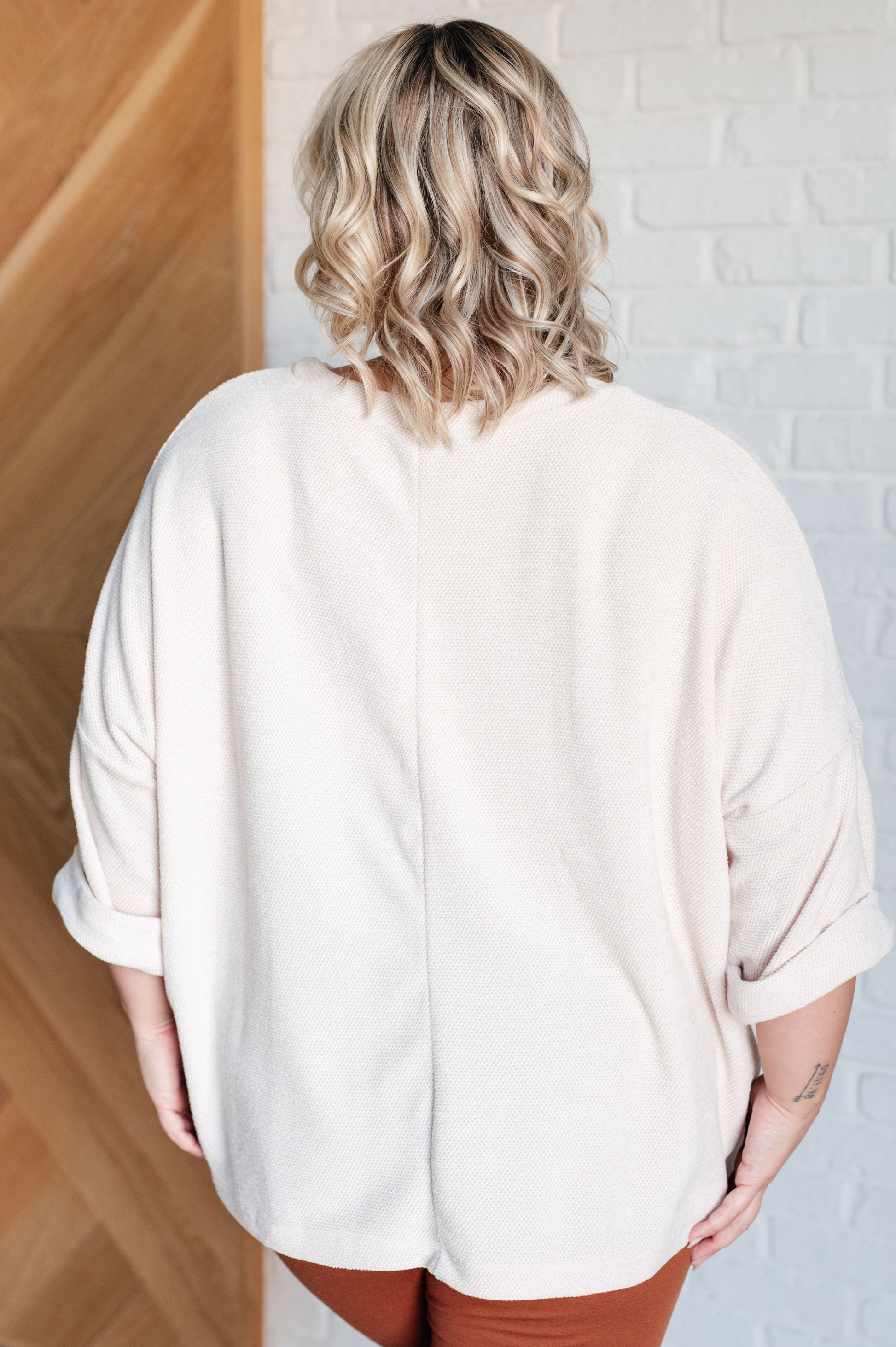 Person wearing a beige oversized shirt in a minimal indoor setting