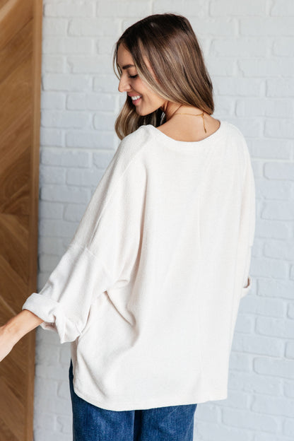 Woman wearing a white blouse and blue jeans against a white brick wall.