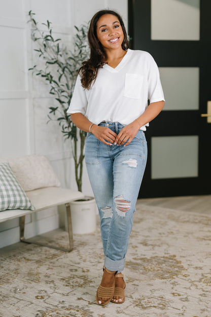 Woman wearing a white shirt and light blue jeans standing in a room with a plant and bench.