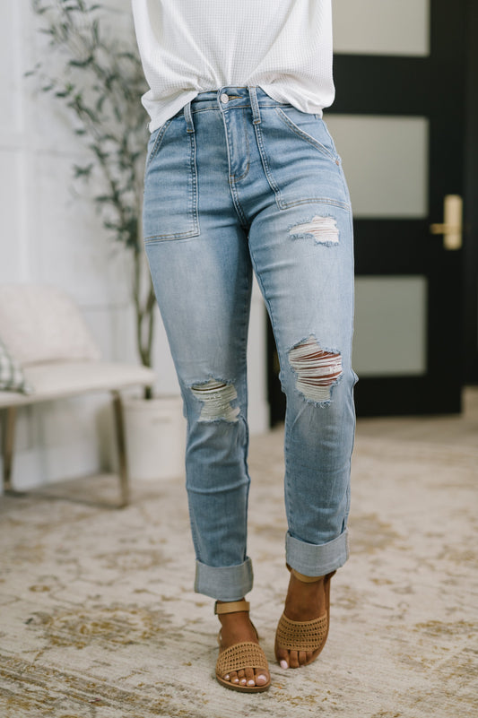 Person wearing light blue distressed jeans with a white top and brown sandals indoors.