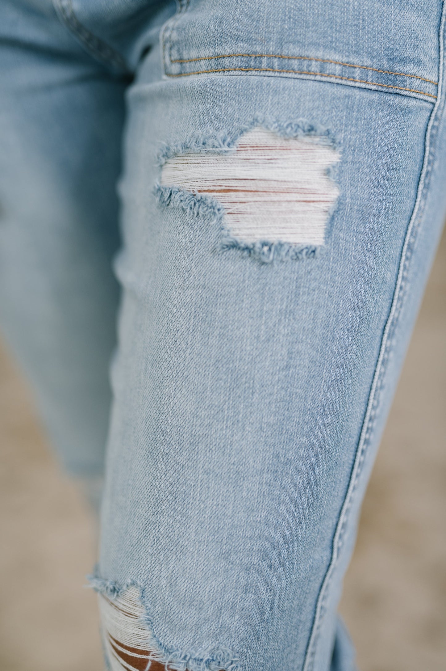 Close-up of a distressed denim knee with a blurred background