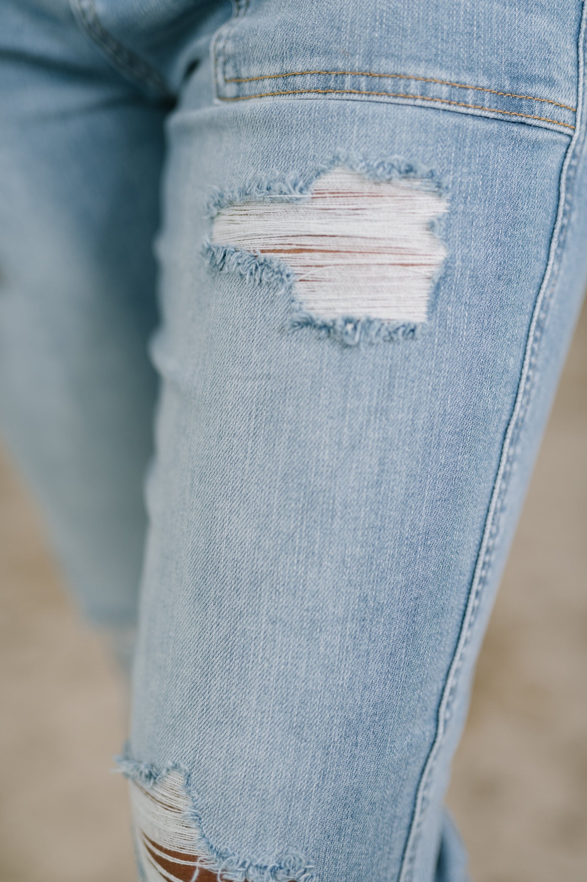 Close-up of a distressed denim knee with a blurred background