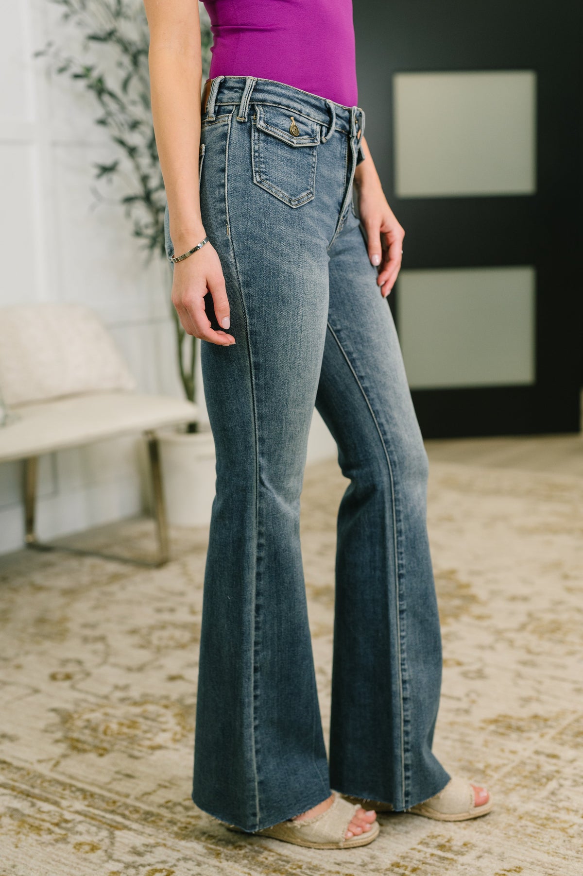Person wearing blue flared jeans and a purple top in an indoor setting.
