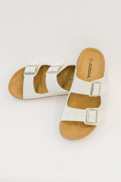 Pair of white sandals with brown soles on a light gray background