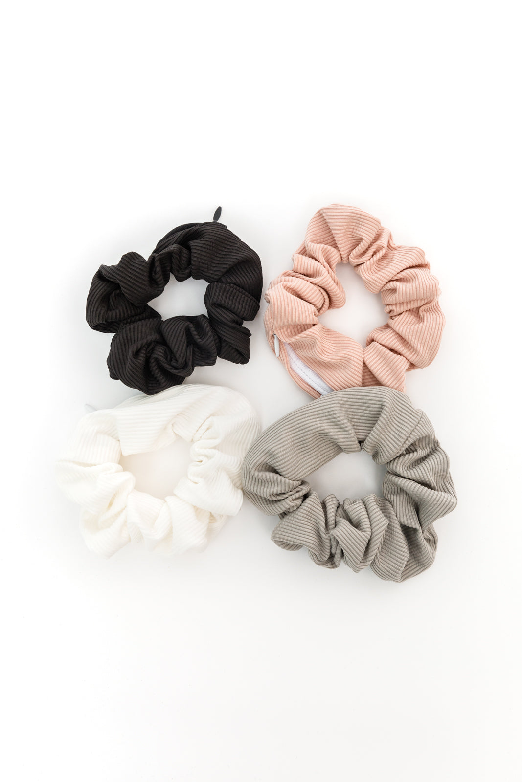 Four scrunchies in black, pink, white, and beige on a white background