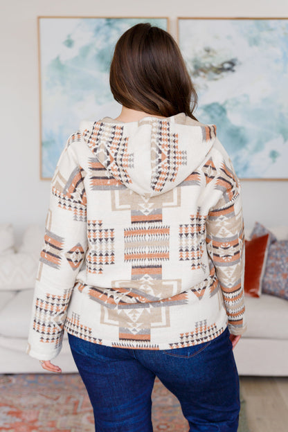 Person wearing a patterned hoodie in a living room setting