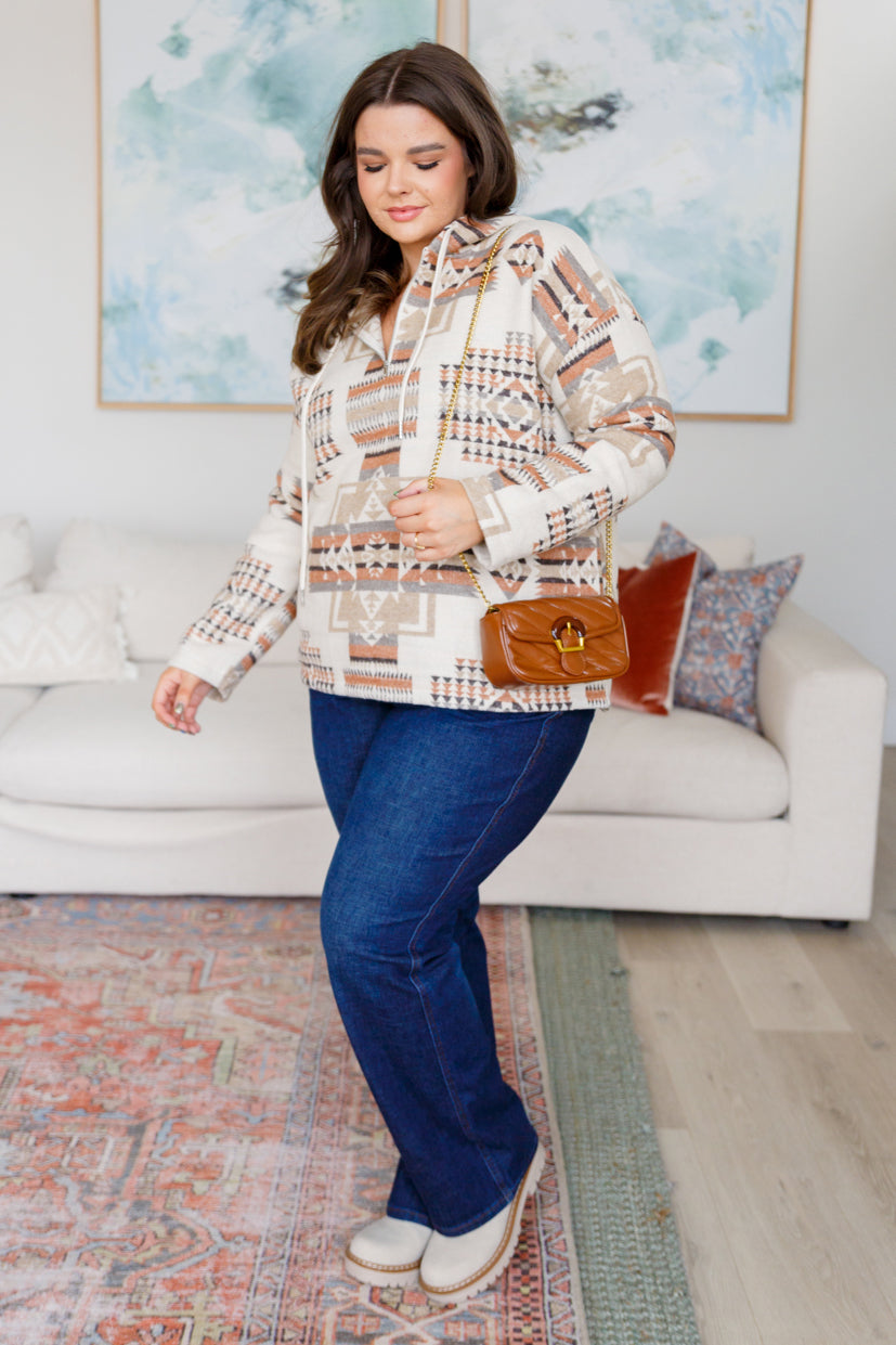 Woman in a patterned blouse and blue jeans standing in a living room.