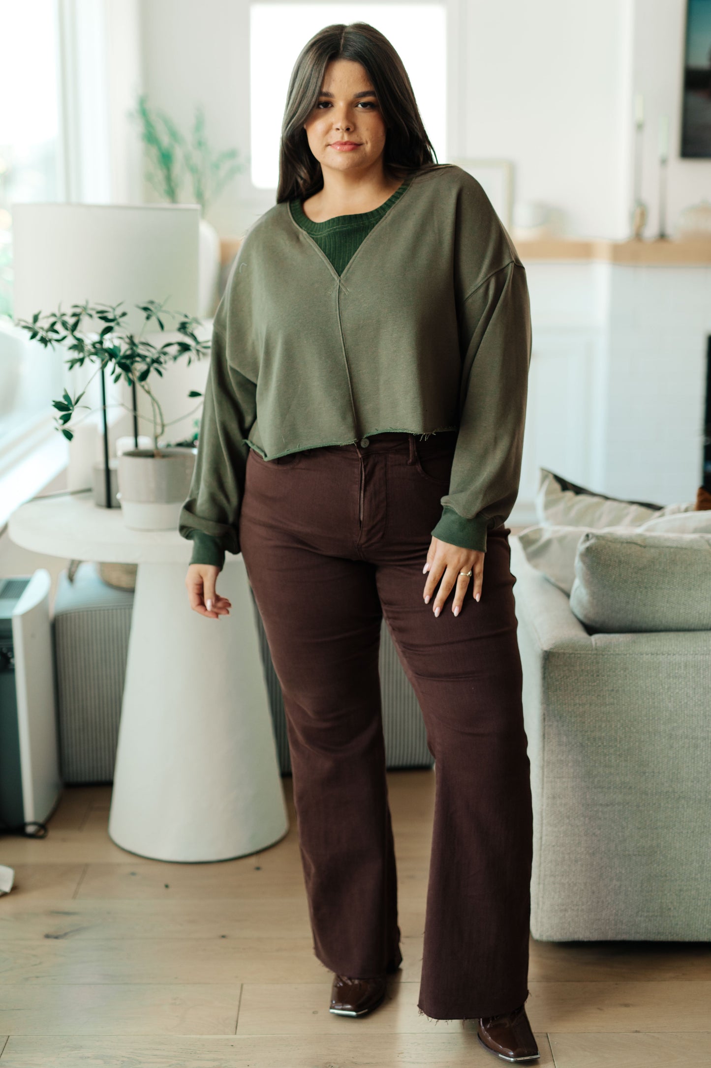 Woman wearing a green cardigan and brown pants in a living room setting