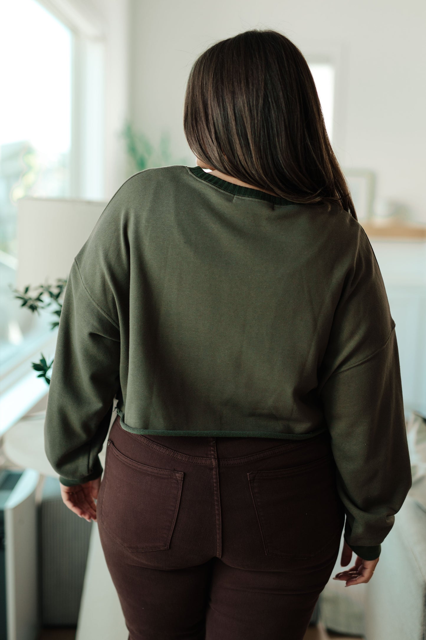 Person wearing an olive green sweatshirt and brown pants in a bright room.