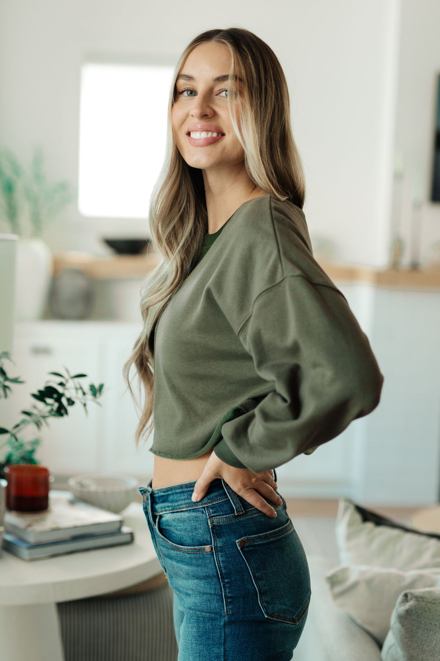 Woman wearing a green sweater and blue jeans in a modern living room.