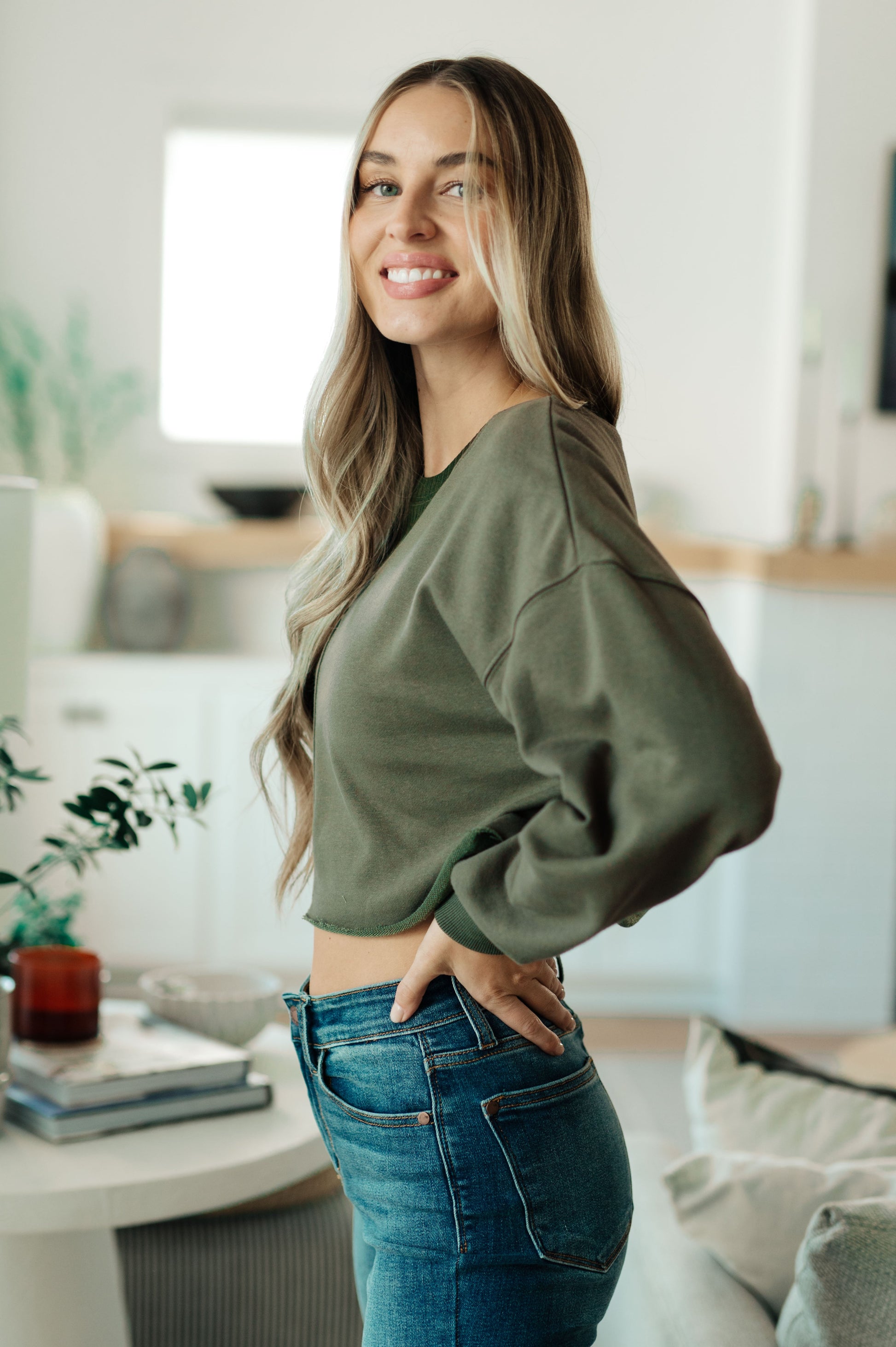 Woman wearing a green sweater and blue jeans in a modern living room.