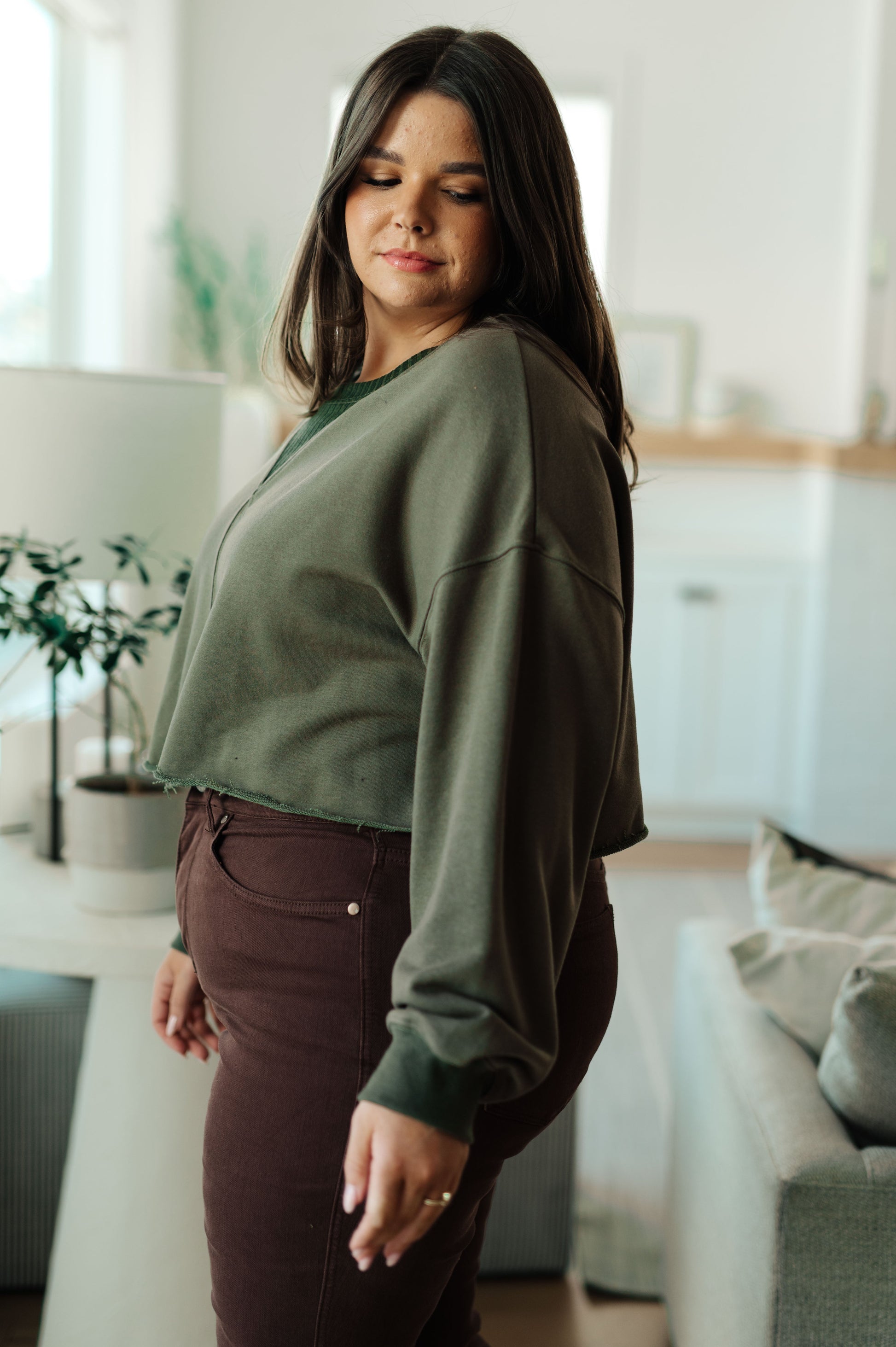Woman wearing a green sweater and brown pants in a living room.