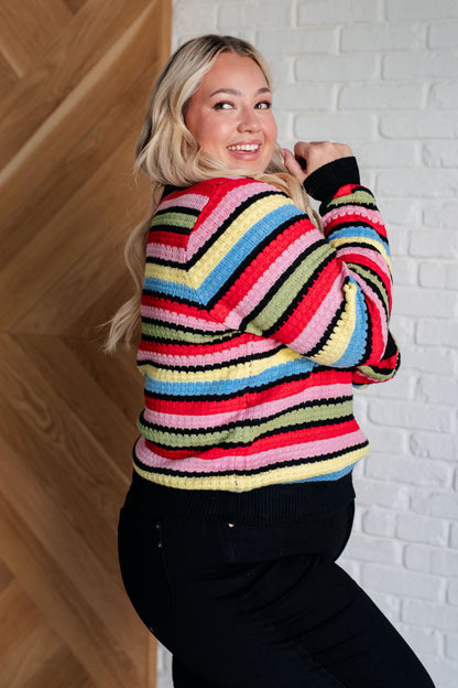 Woman wearing a colorful striped sweater against a white brick wall.