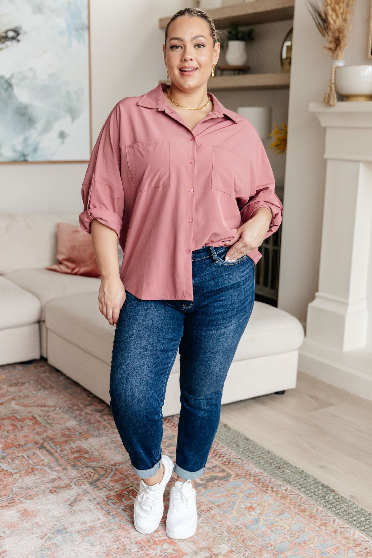 Woman wearing a pink shirt and blue jeans standing in a living room.