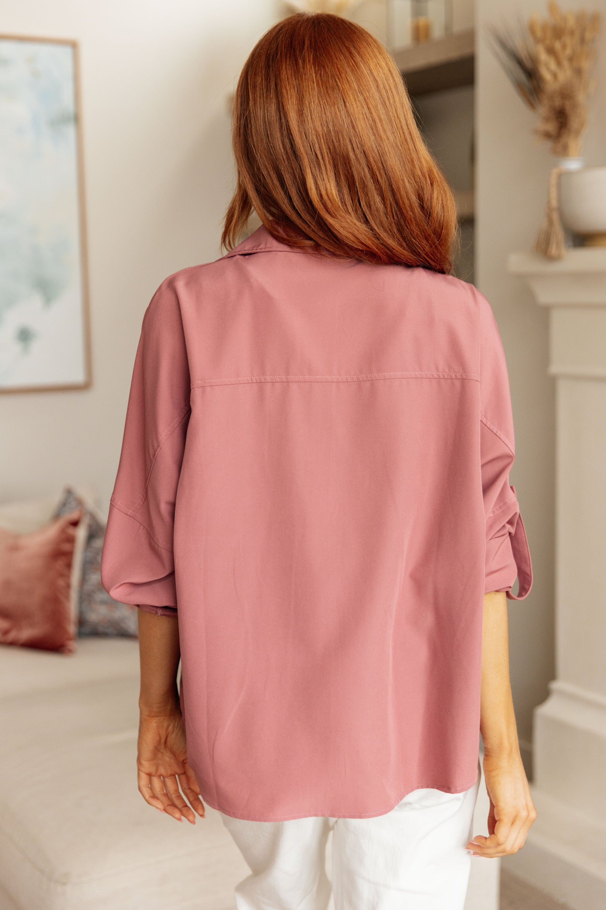 Person wearing a pink shirt in a room with a couch and decorative items.