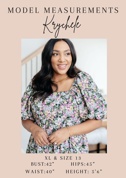 A promotional measurement graphic for a floral dress model, with the text 'MODEL MEASUREMENTS' and 'Krychelle' at the top, a portrait of a woman wearing the dress in the center, and sizing details for XL & Size 13 listed at the bottom on a beige background.