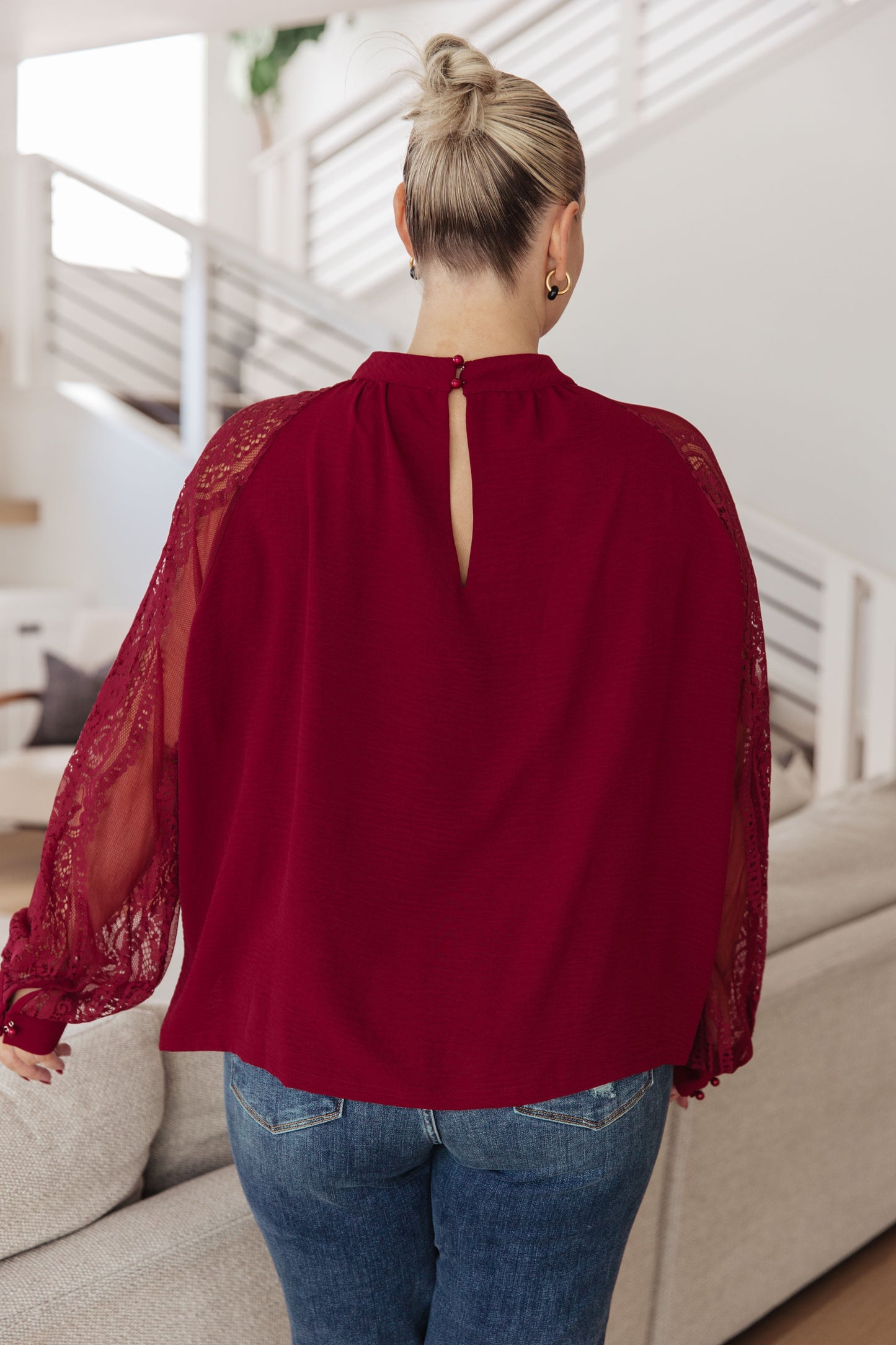 Woman wearing a burgundy blouse with lace sleeves in a living room setting