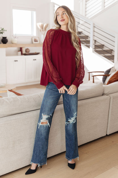 Woman in a red top and blue jeans standing in a modern living room.