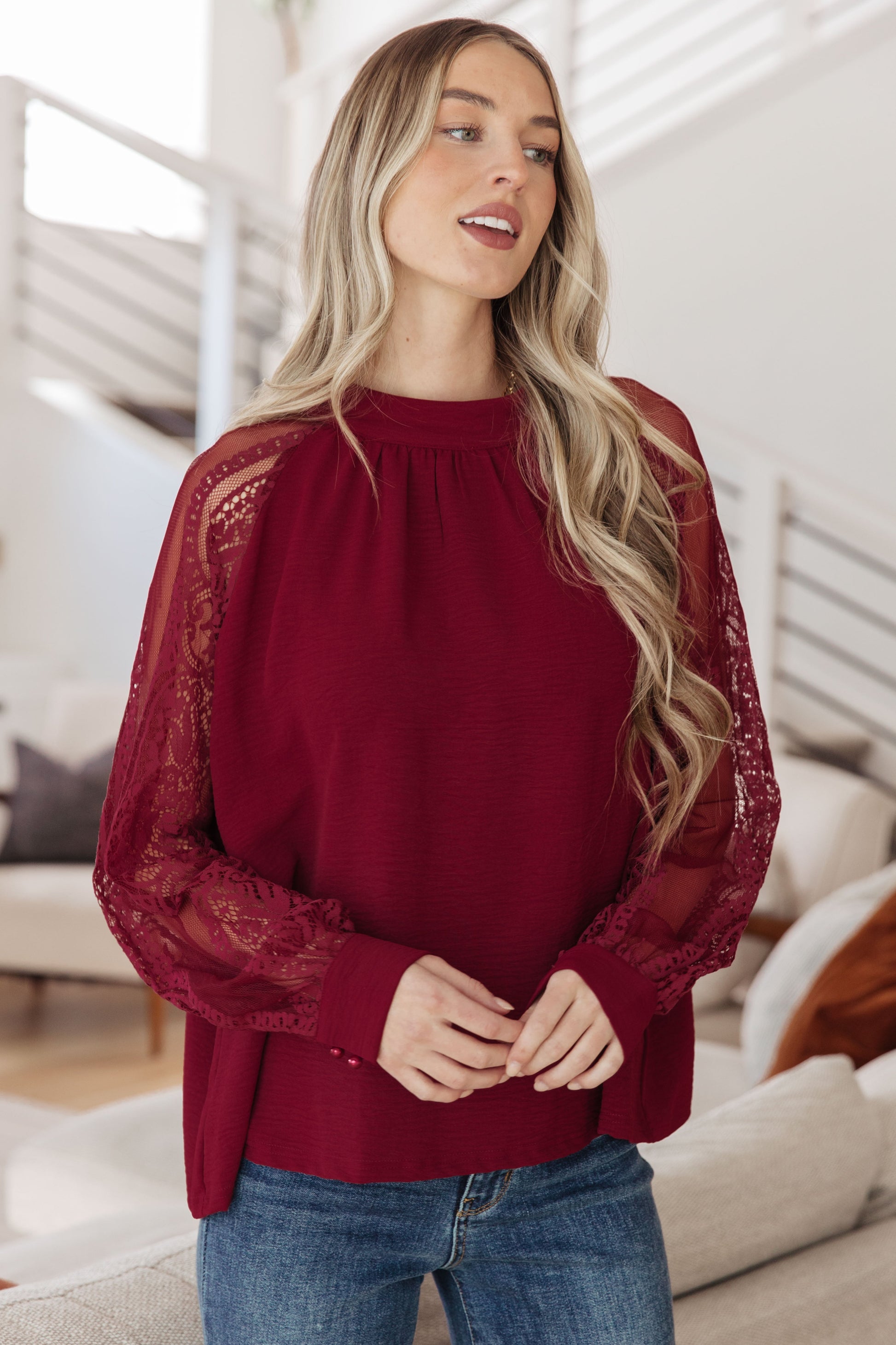 Woman wearing a burgundy blouse with lace sleeves in a living room setting