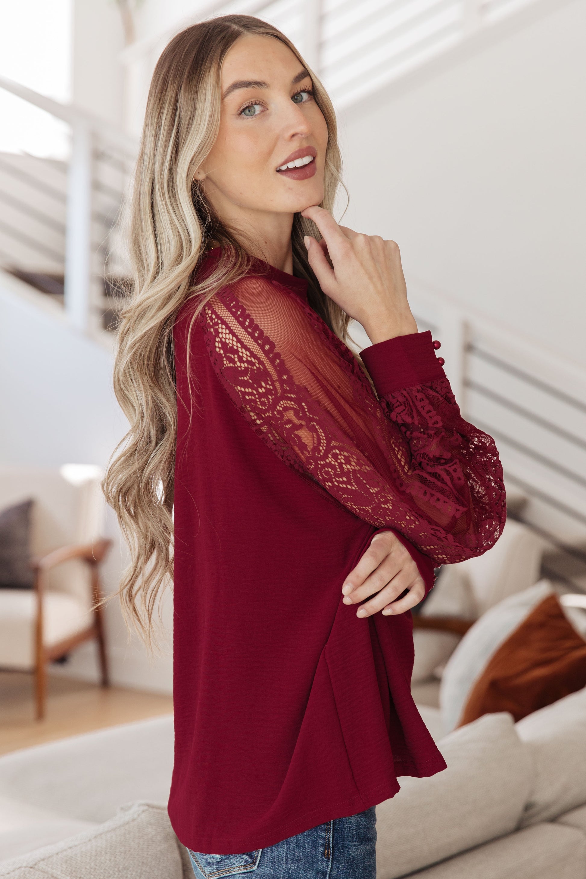 Woman wearing a burgundy blouse with lace sleeves in a living room setting