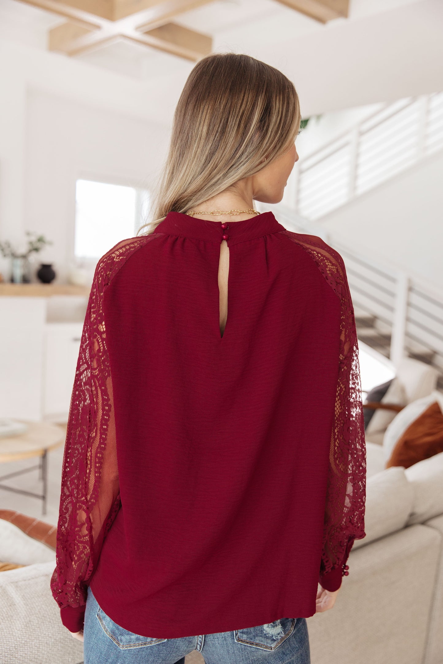 Woman wearing a burgundy blouse with lace sleeves in a modern living room.