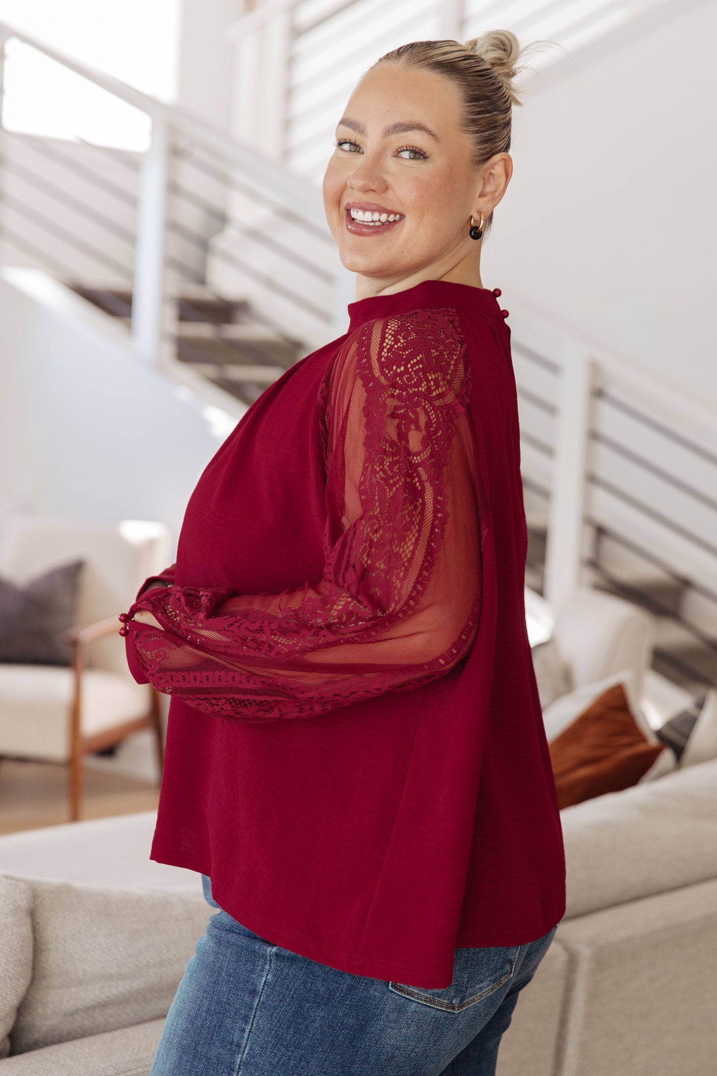 Woman wearing a red blouse with lace detailing in a modern living room.