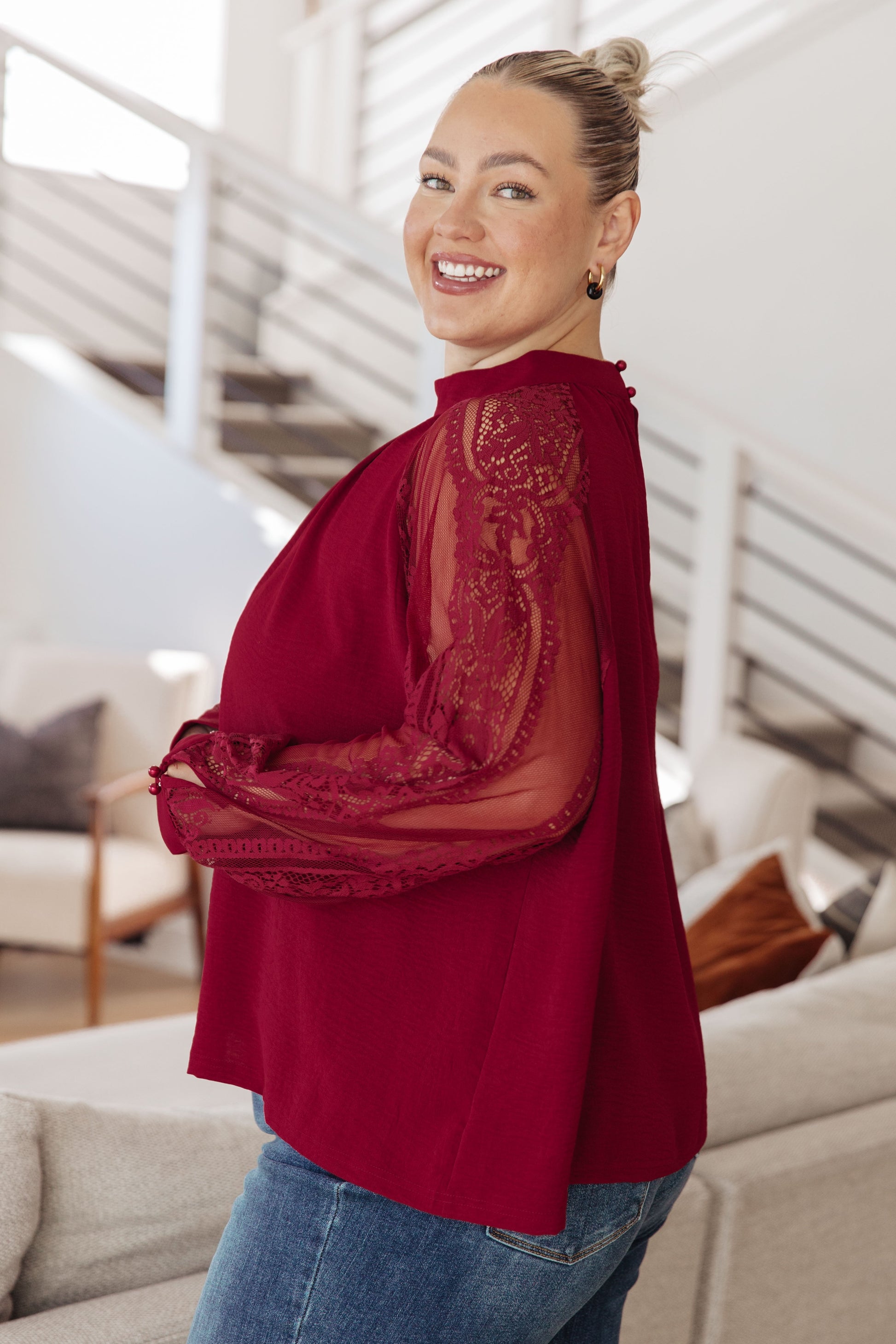 Woman wearing a red blouse with lace detailing in a modern living room.