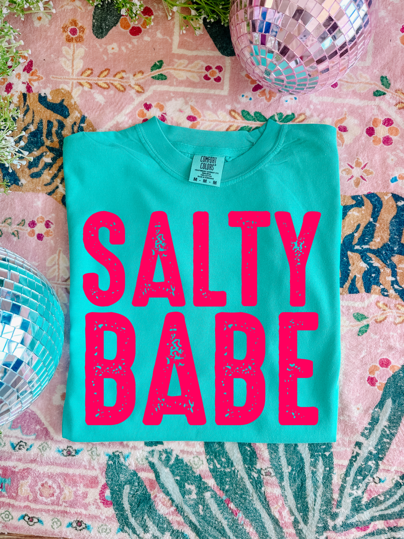 Turquoise t-shirt with 'Salty Babe' in pink on a colorful patterned surface