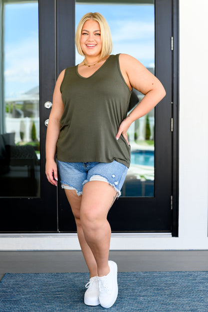 A woman wearing an olive green tank top with a laser cut flag design on the back, in a v-neckline cut.