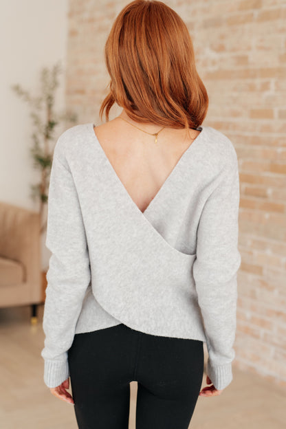 Woman wearing a light gray sweater with an open back in a casual indoor setting.