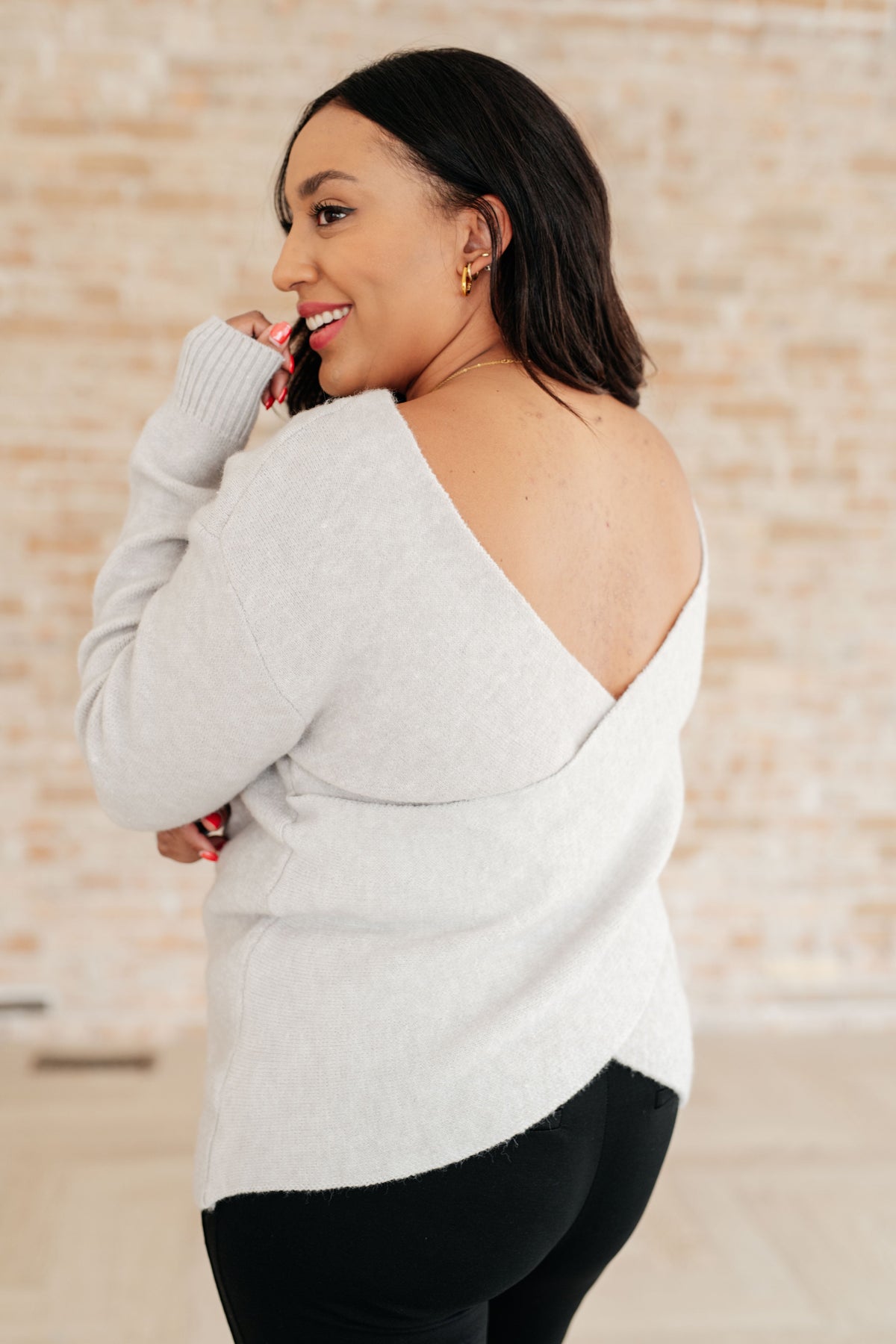 Woman wearing a light gray sweater with a unique cutout design on a neutral background